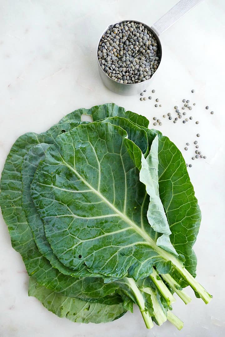 collard greens and a cup of dried green lentils on a counter next to each other