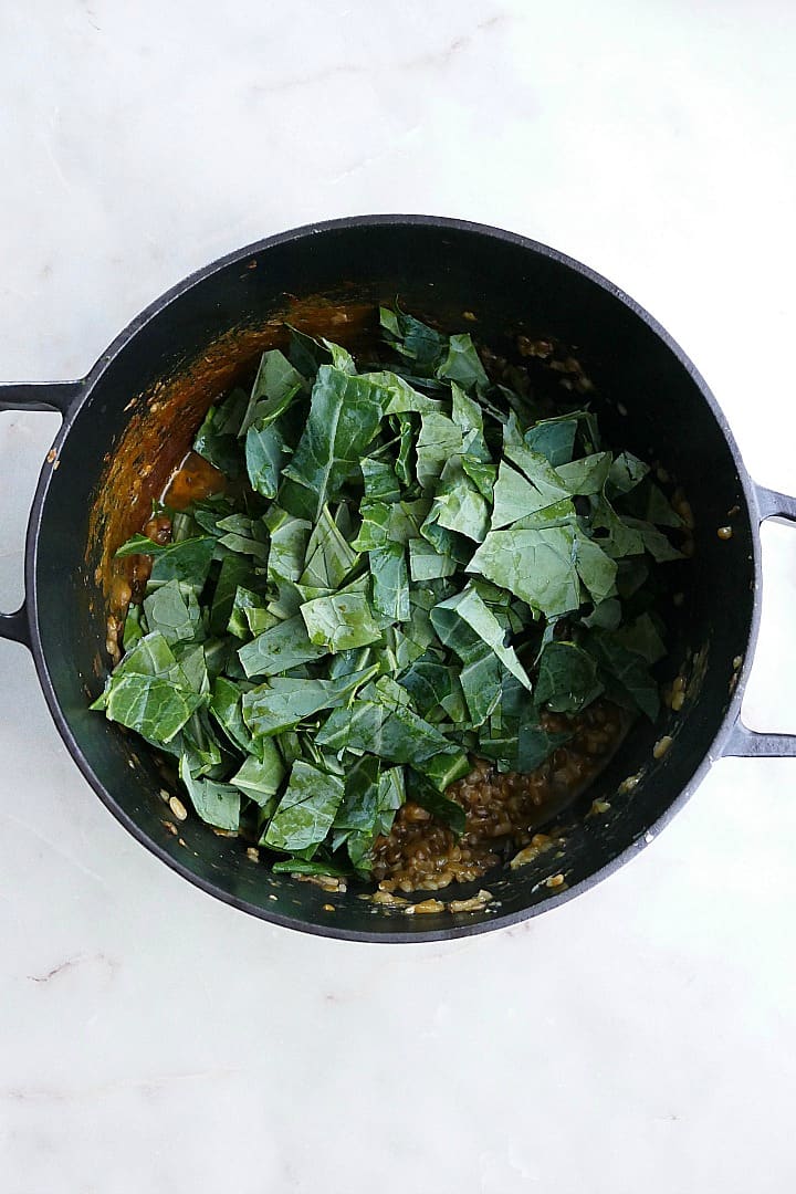 sliced collard greens on top of a risotto in a Dutch oven on a counter