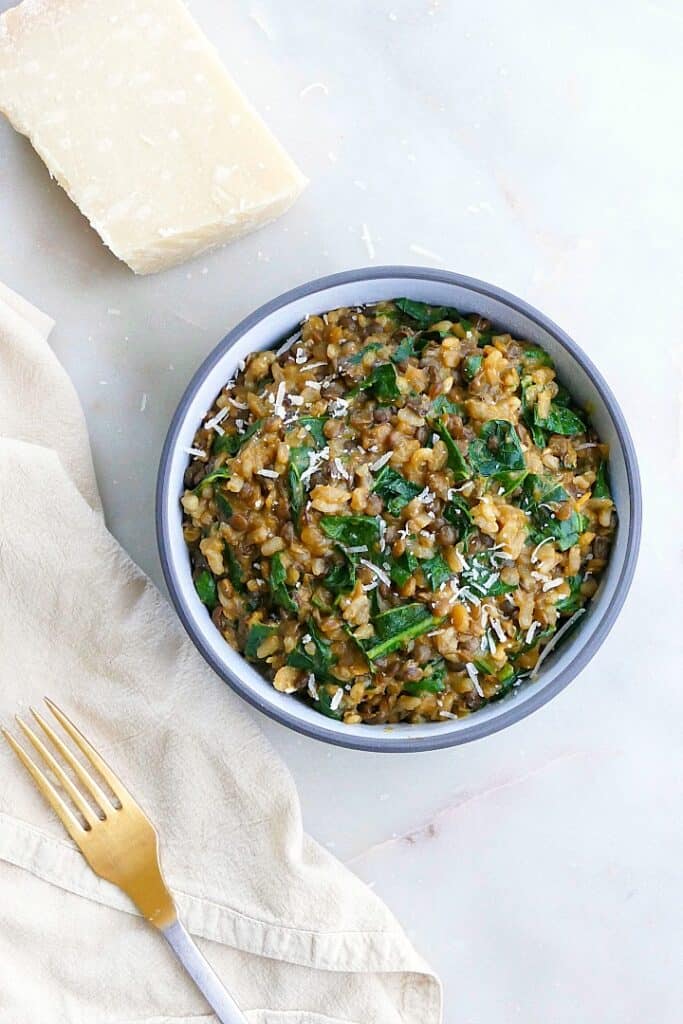 lentil risotto with collard greens on a counter next to a fork and parmesan