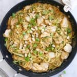 peanut zucchini noodles with chicken in a black skillet topped with scallions