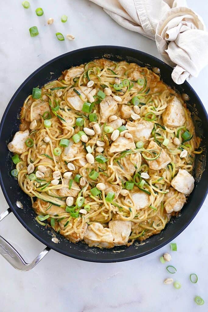 peanut zucchini noodles with chicken in a black skillet topped with scallions
