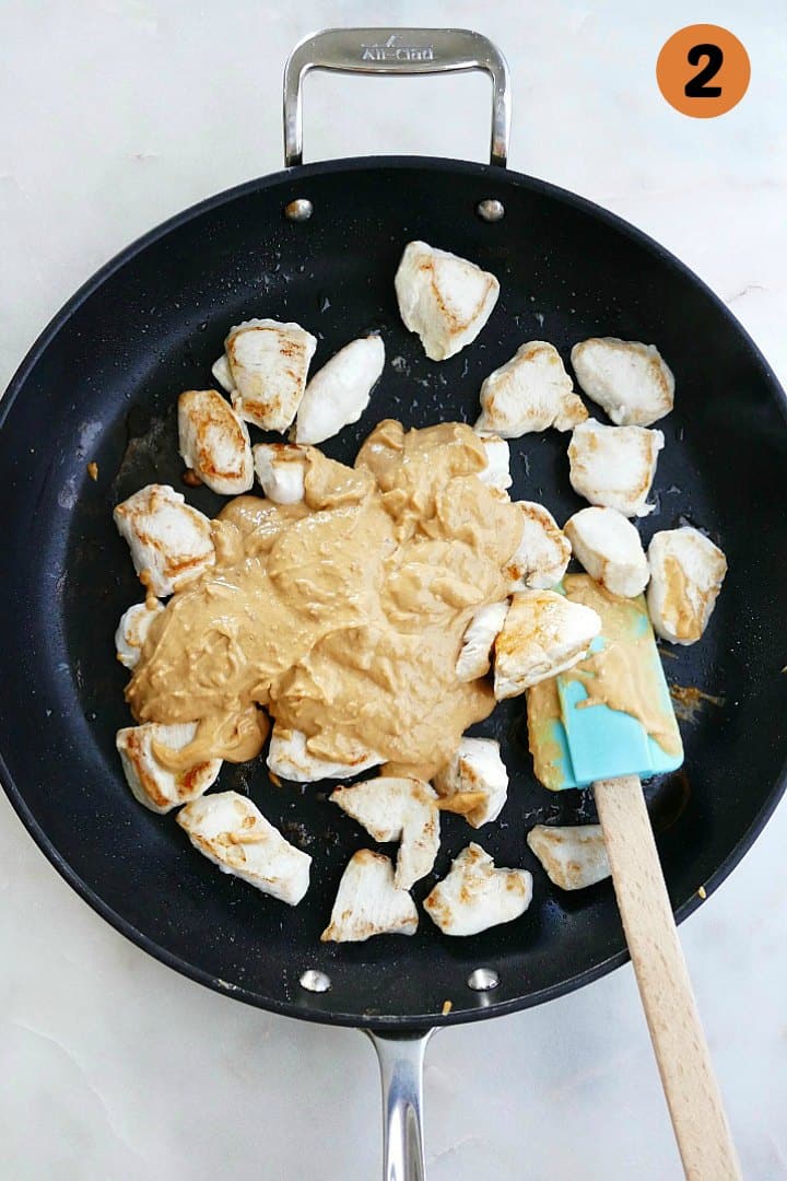 diced chicken cooking in a skillet covered in peanut sauce