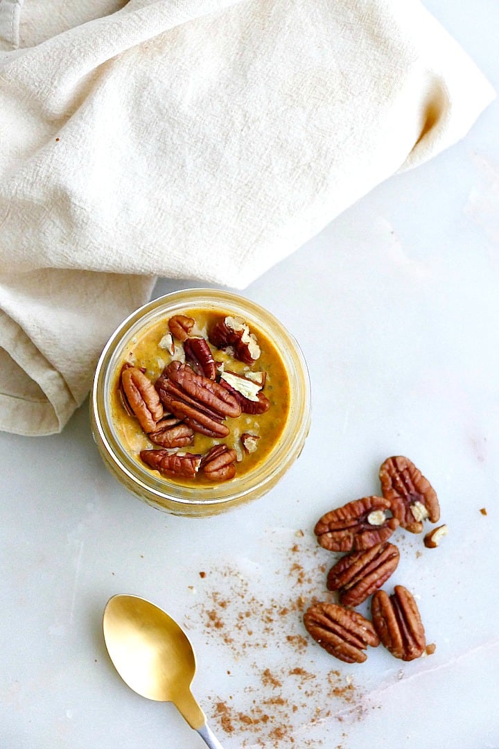 pumpkin chia pudding in a jar next to pecans, a spoon, and a napkin
