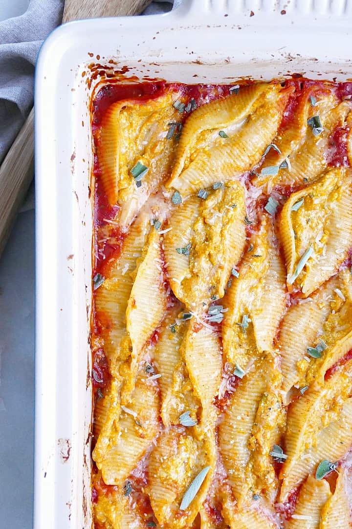 close-up image of pumpkin stuffed shells in a baking dish with fresh herbs and cheese on top