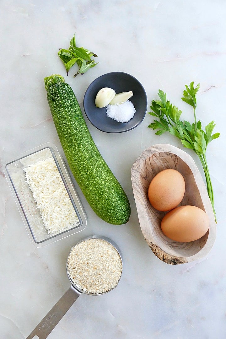 zucchini, garlic, herbs, eggs, bread crumbs, and parmesan cheese on a counter