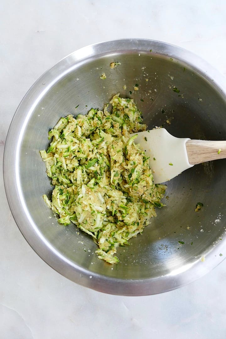 mixture for zucchini balls in a metal mixing bowl with a rubber spatula