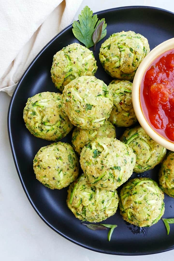 close up of zucchini bites on a black serving plate with tomato sauce