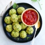 square image of zucchini balls on a serving plate with a bowl of tomato sauce