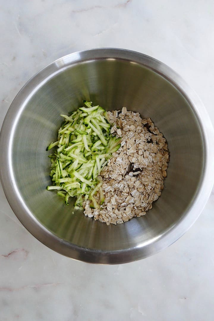 shredded zucchini, oats, cinnamon, walnuts, and raisins in a metal mixing bowl