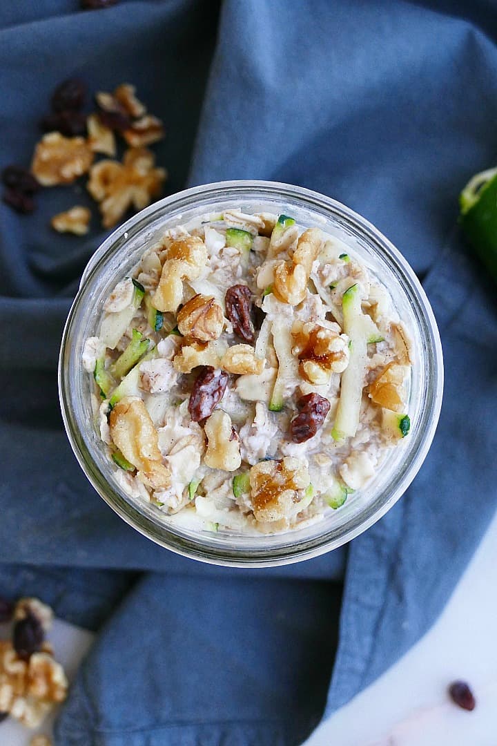 overhead shot of zucchini overnight oats in a jar topped with walnuts and raisins
