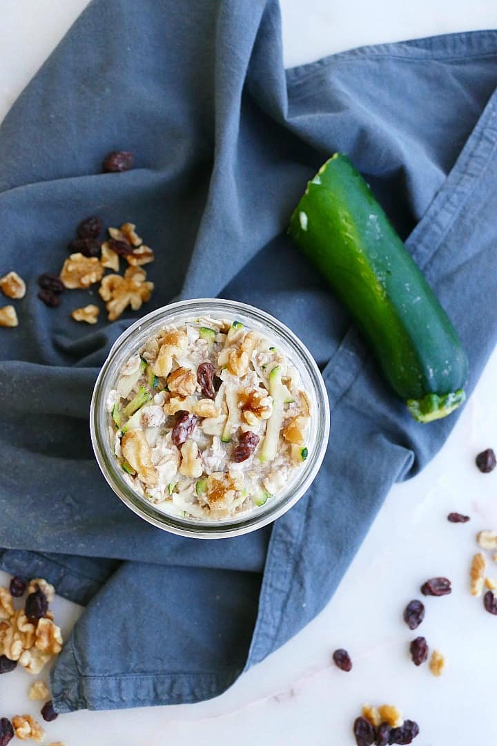 overhead shot of zucchini overnight oats on a napkin next to zucchini, walnuts, and raisins