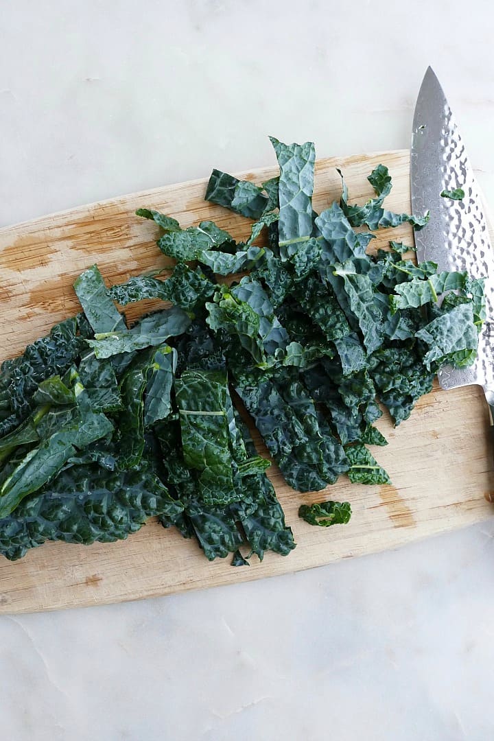 thinly sliced kale on a bamboo cutting board with a chef's knife