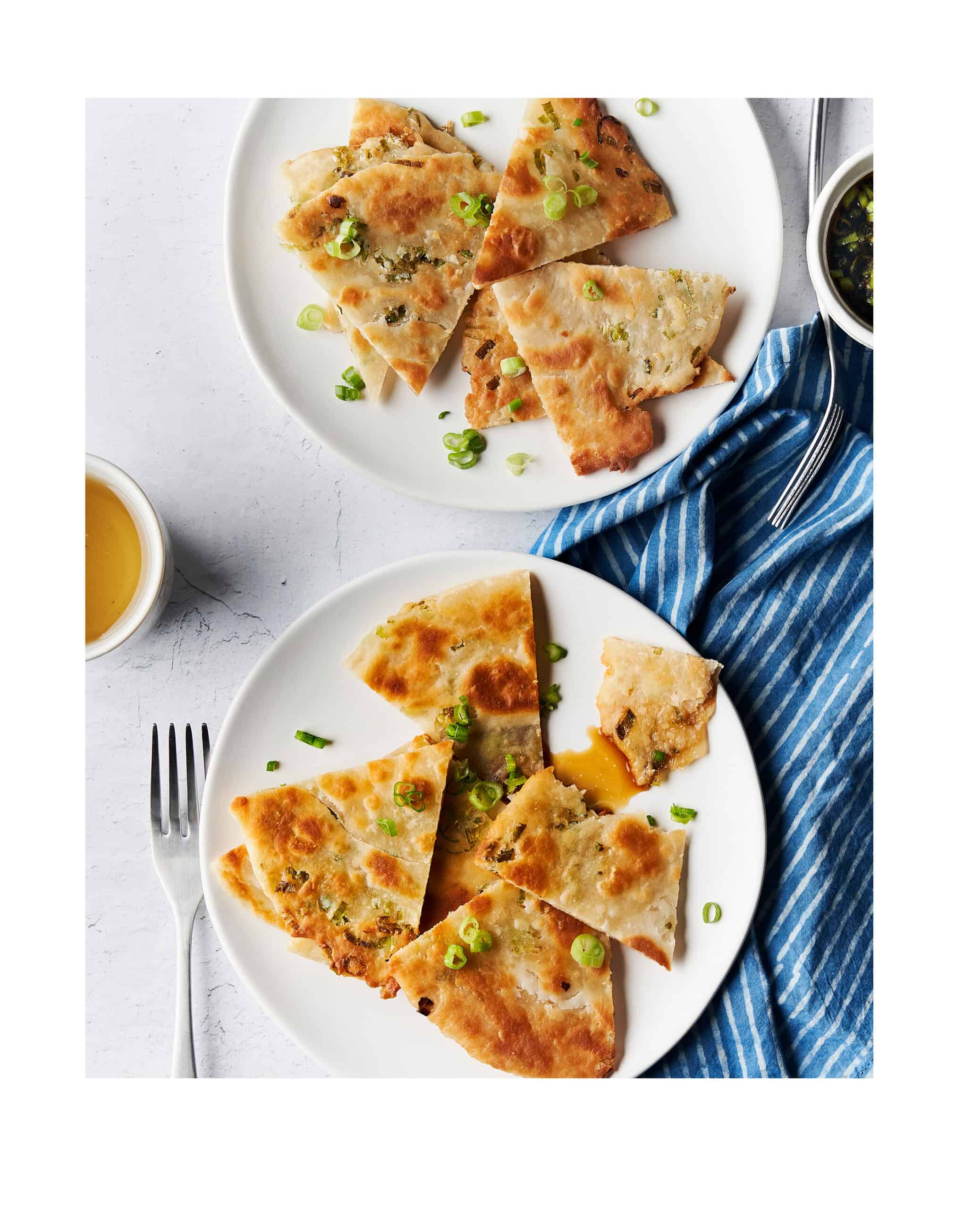homemade scallion pancakes on white serving plates on a counter with a napkin