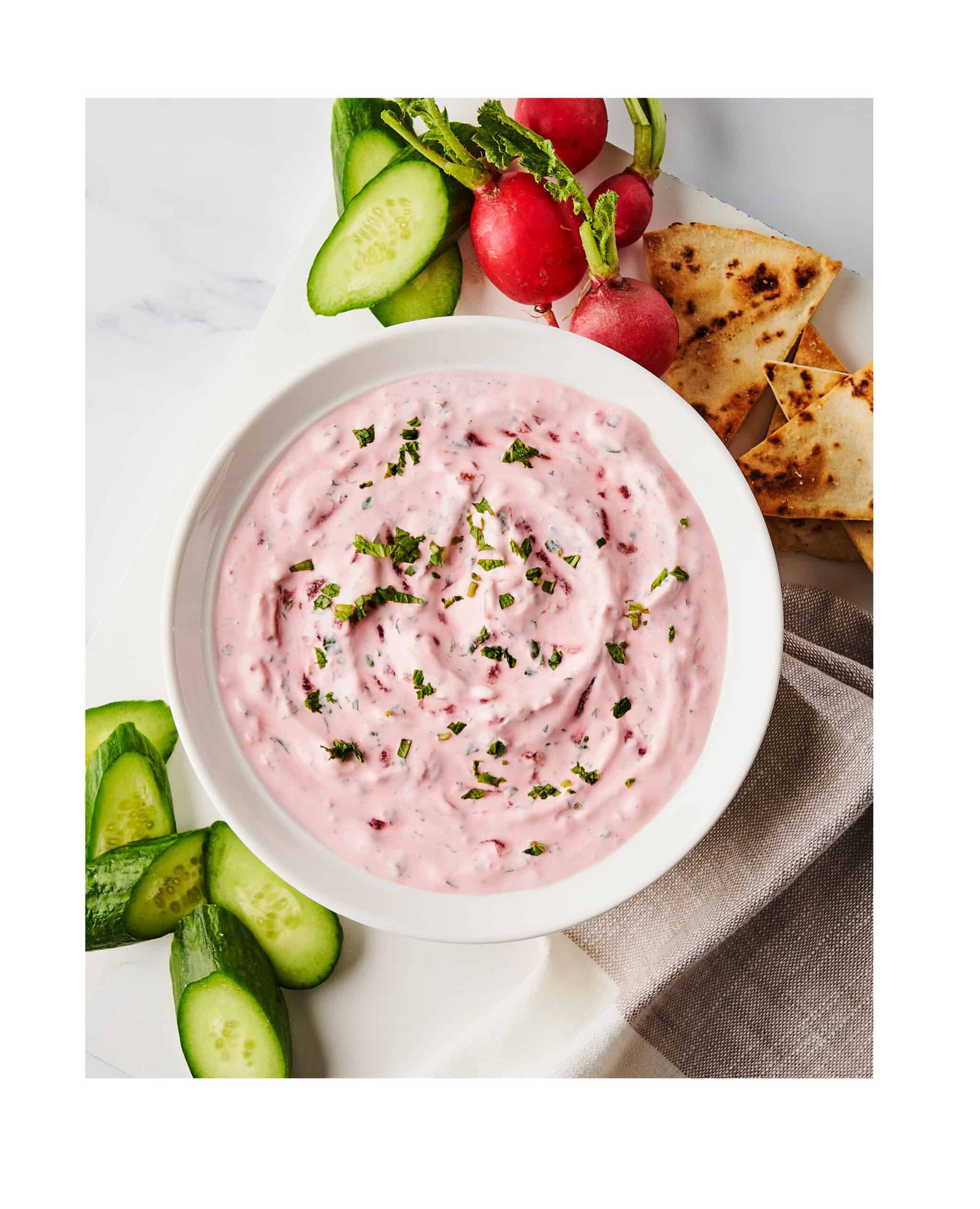 beet yogurt dip with mint in a bowl surrounded by veggies and chips