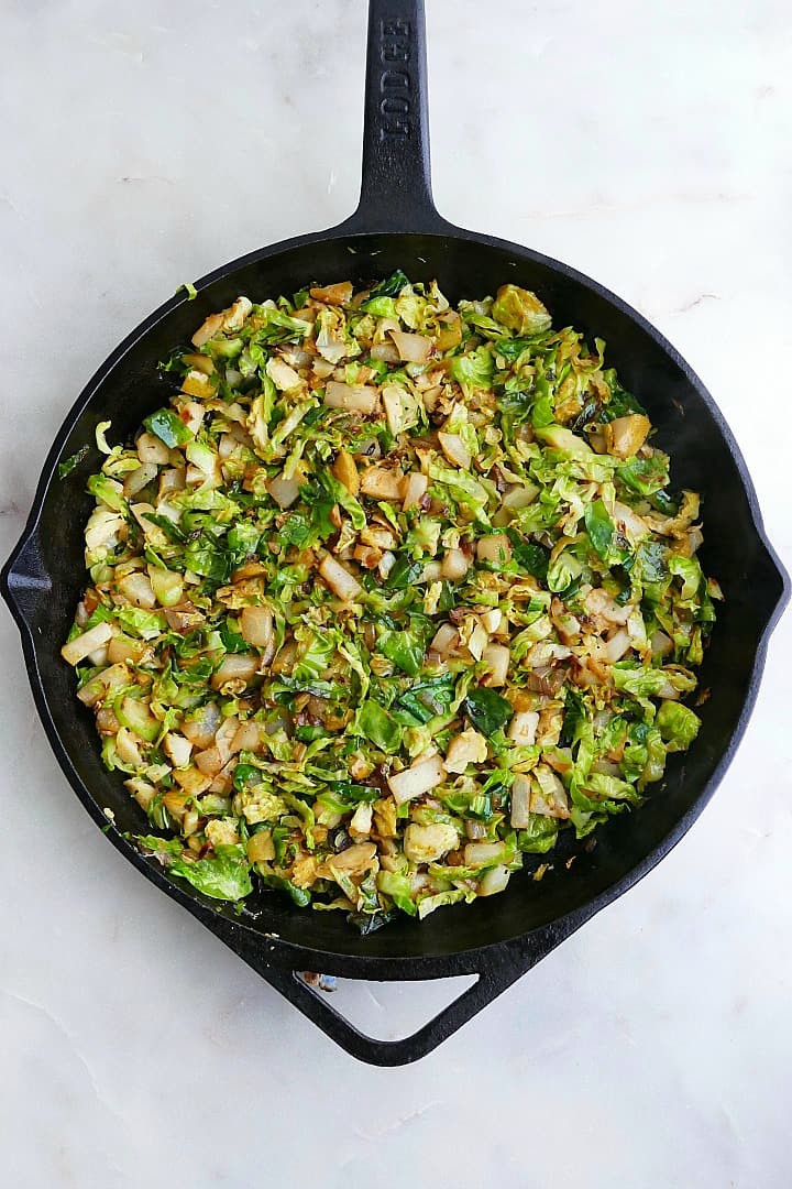 shredded brussels sprouts, pears, and shallots cooked down in a large cast iron skillet on a counter