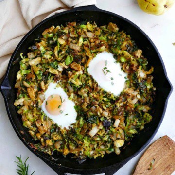 cast iron skillet with sauteed brussels sprouts and fried eggs on a counter next to serving spoon