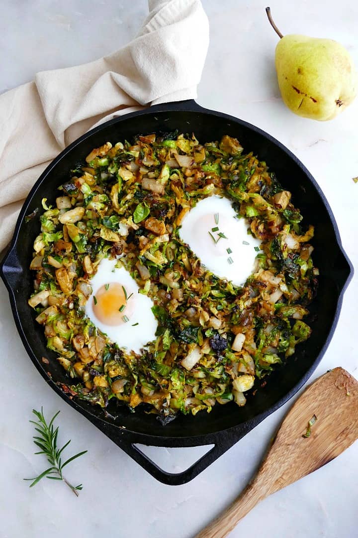 cast iron skillet with sauteed brussels sprouts and fried eggs on a counter next to spoon