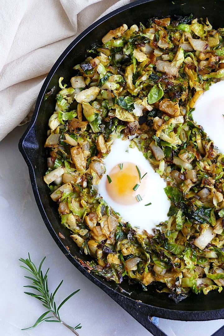 cooked Brussels sprouts and eggs breakfast hash topped with rosemary on a counter