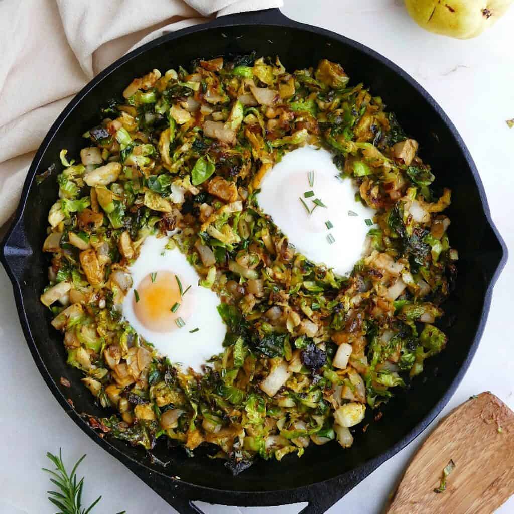 square image of Brussels sprouts and eggs hash in a cast iron skillet on a counter