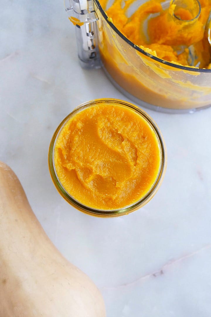 butternut squash puree in a glass jar on a counter next to food processor