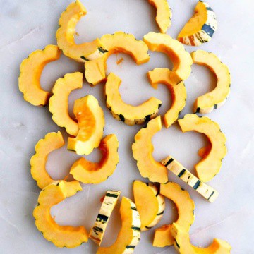 delicata squash cut into half-moon shapes spread out on a white counter
