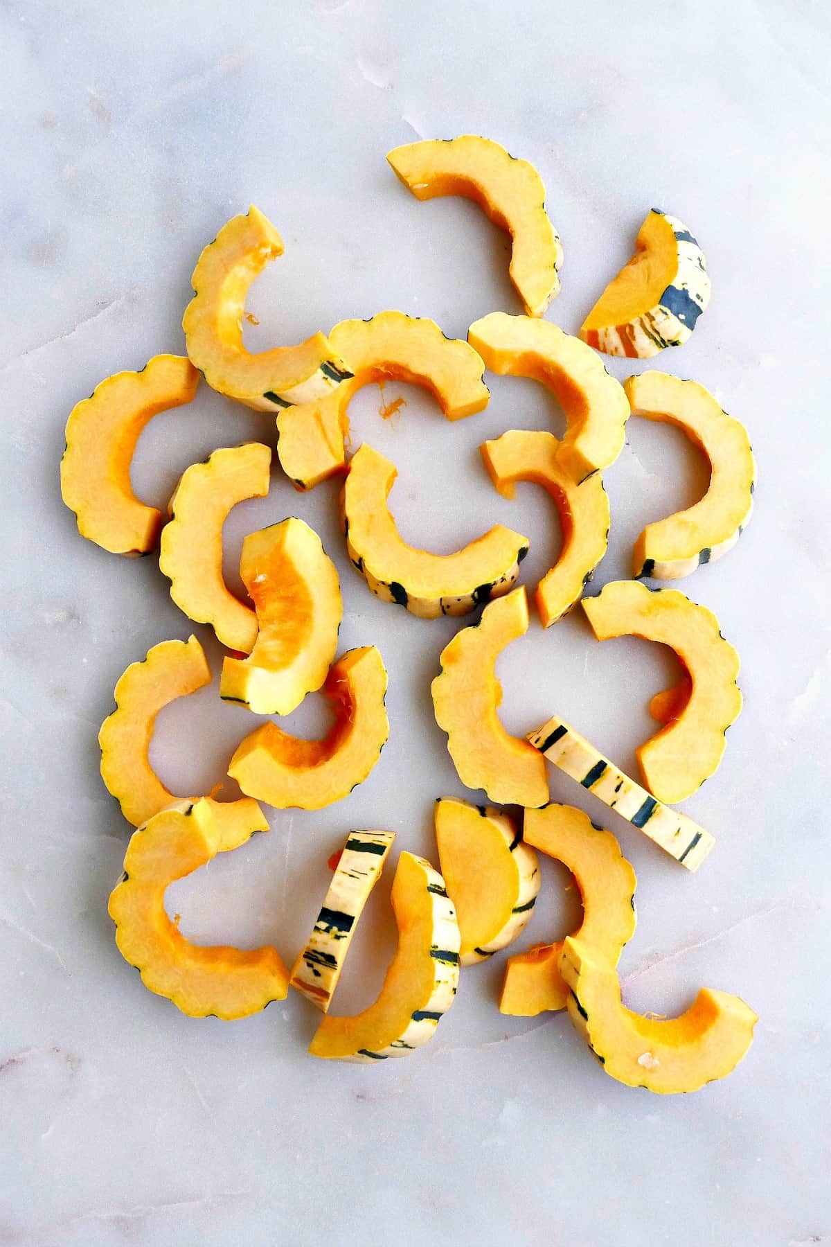 delicata squash cut into half-moon shapes spread out on a white counter
