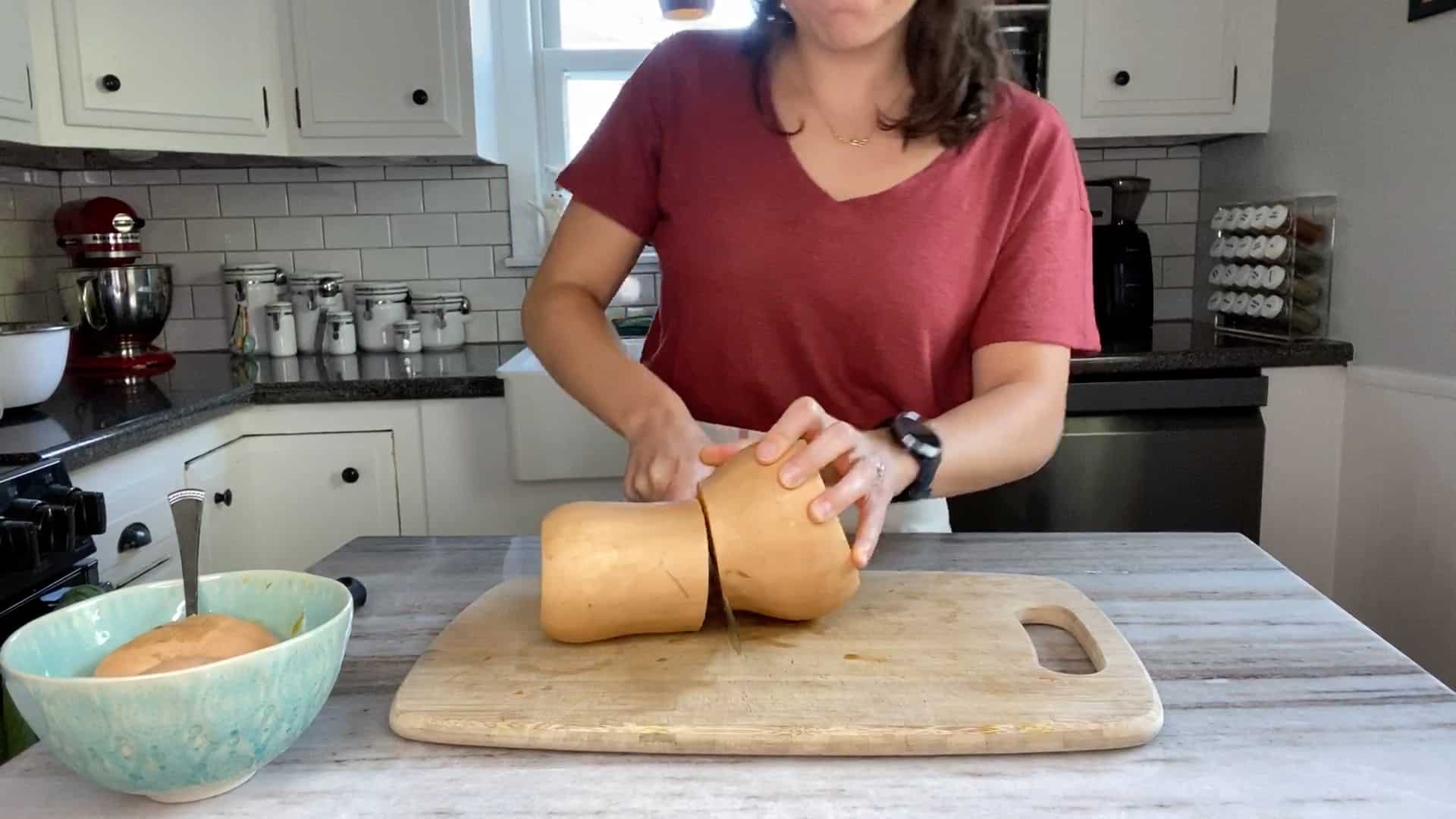 woman cutting a butternut squash in half on top of a cutting board in a kitchen
