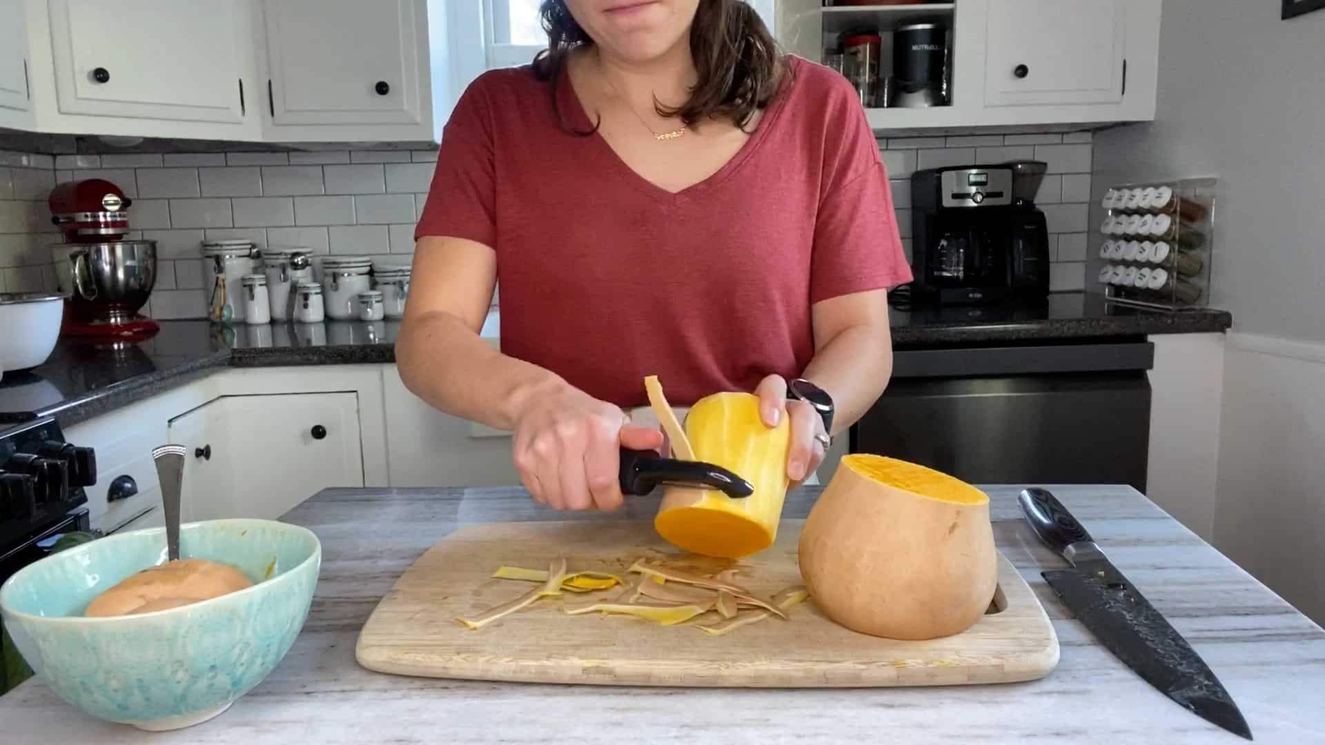 woman peeling butternut squash with a swivel peeler over a cutting board