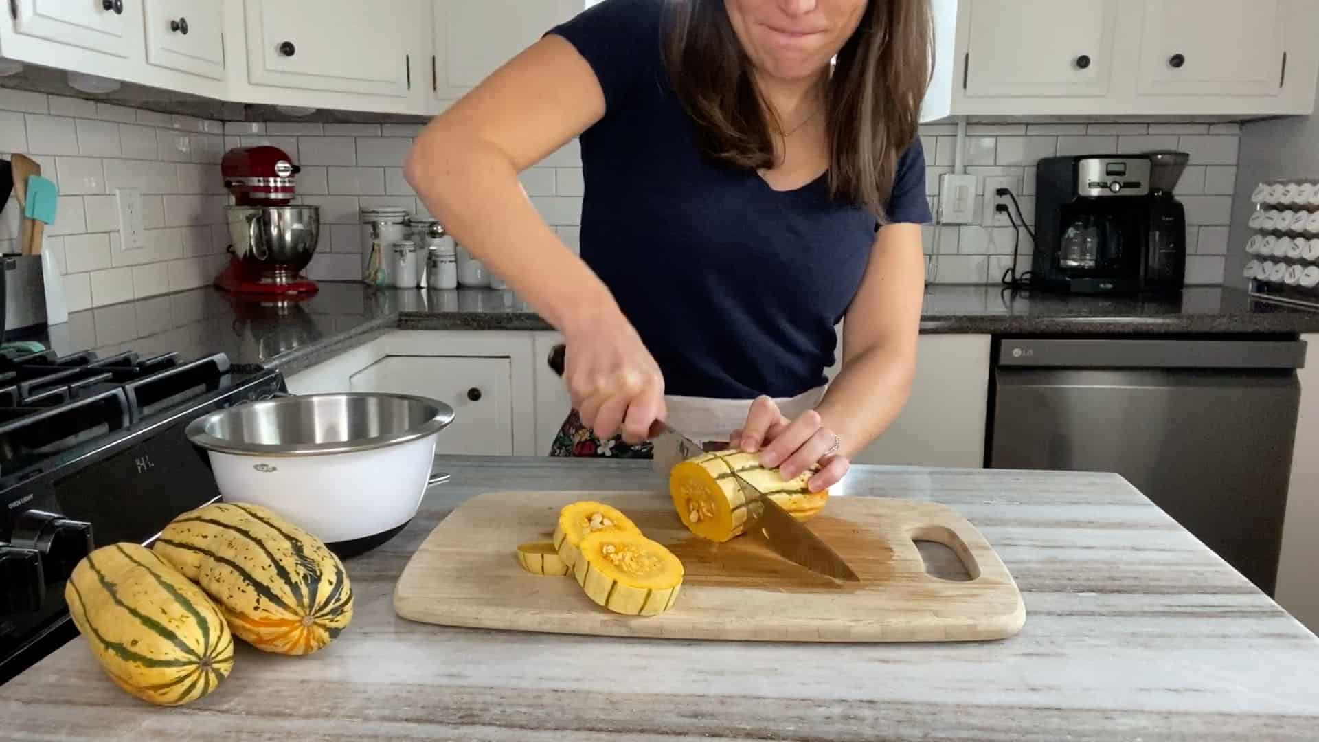 woman cutting delicata squash into rings on a cutting board in a kitchen
