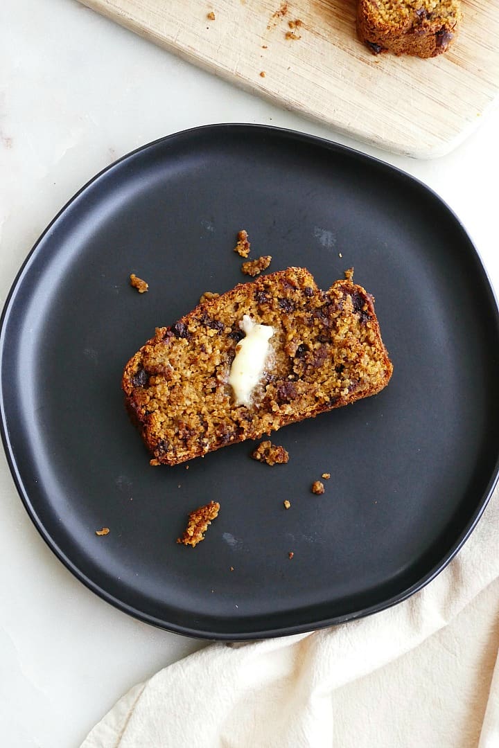 slice of pumpkin oatmeal bread with melted butter on a black plate on a counter