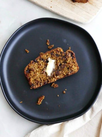 square image of a slice of pumpkin oatmeal bread on a black plate on a counter