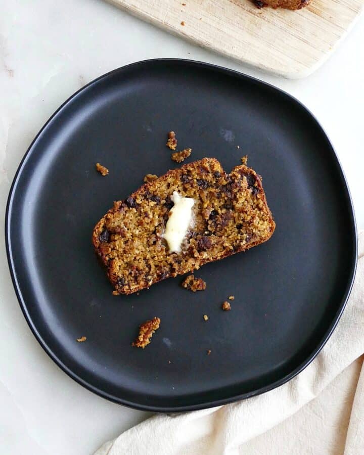 square image of a slice of pumpkin oatmeal bread on a black plate on a counter
