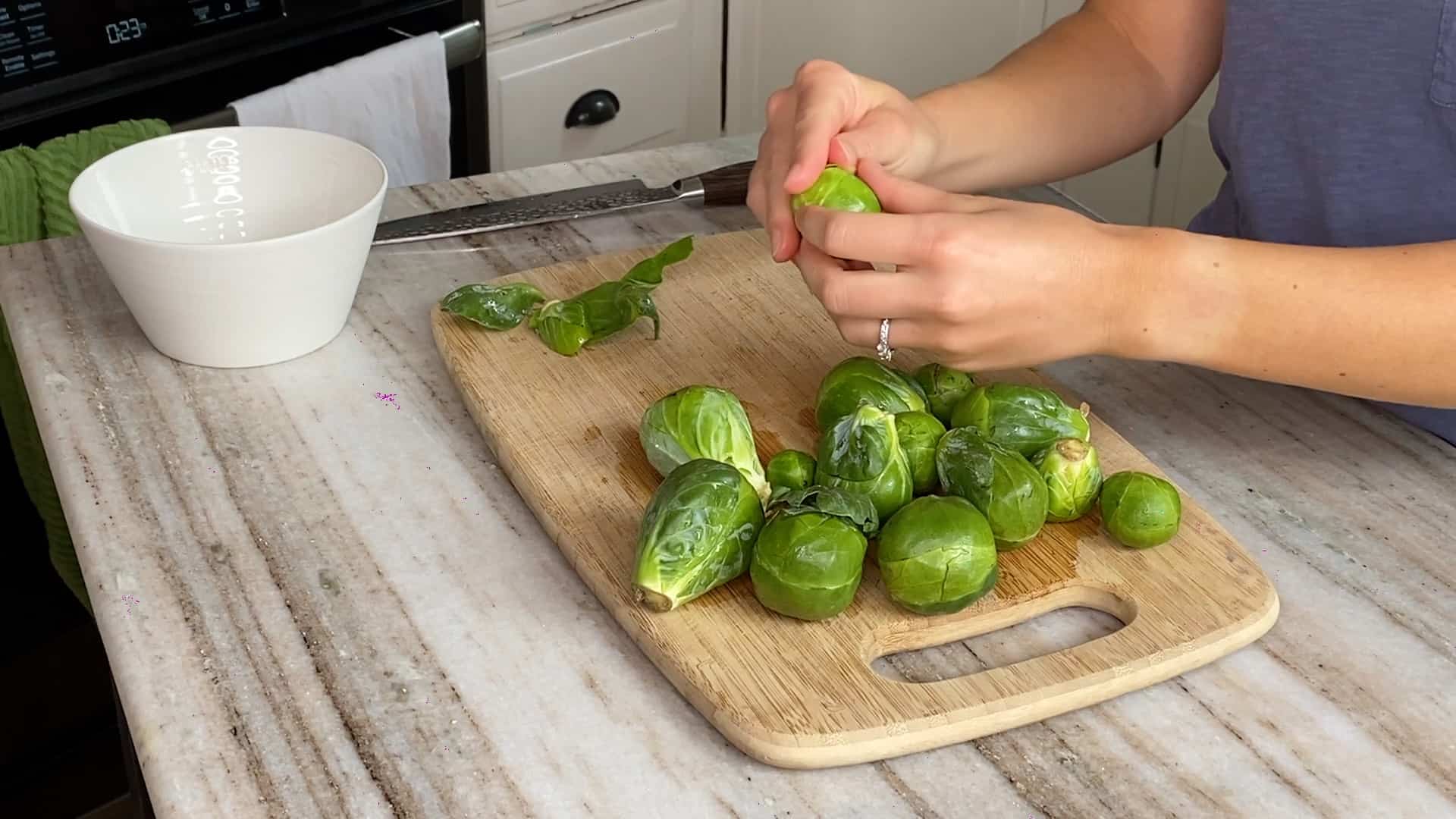 woman's hands holding a Brussels sprout and peeling off leaves