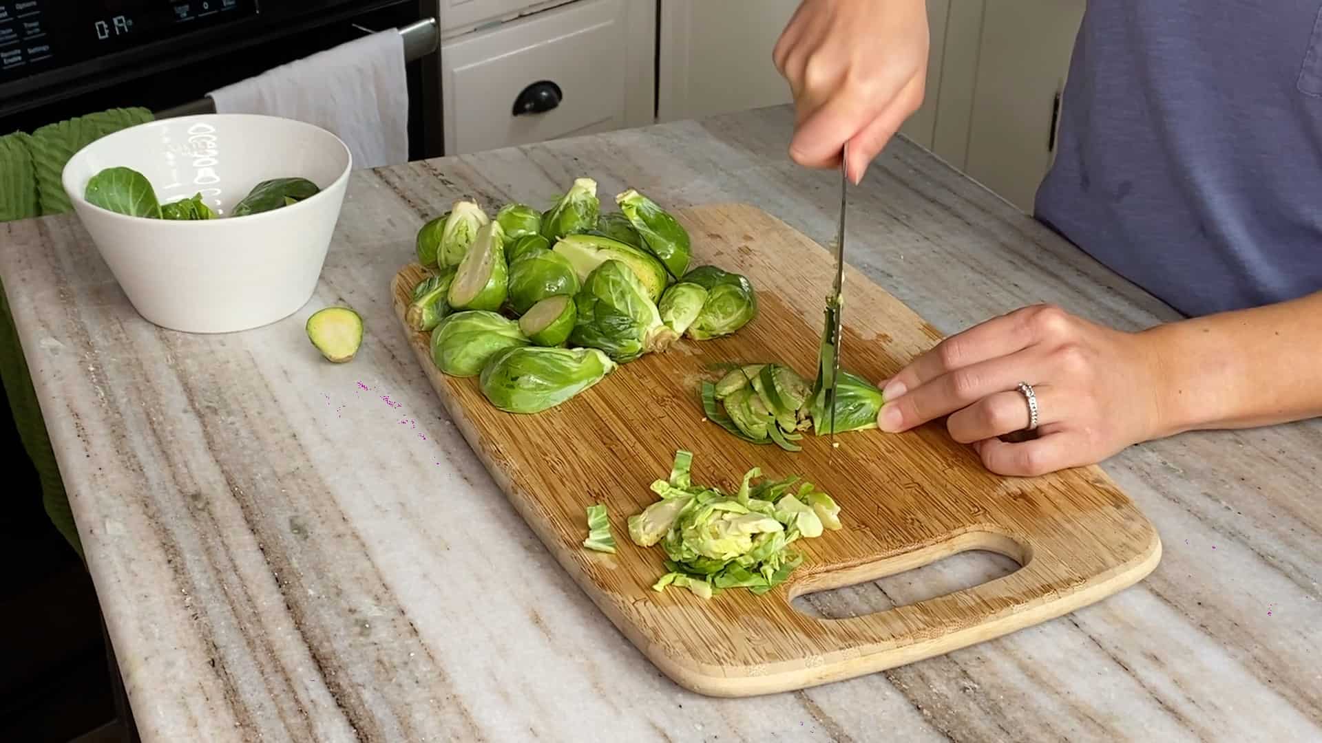 woman slicing Brussels sprouts on a bamboo cutting board