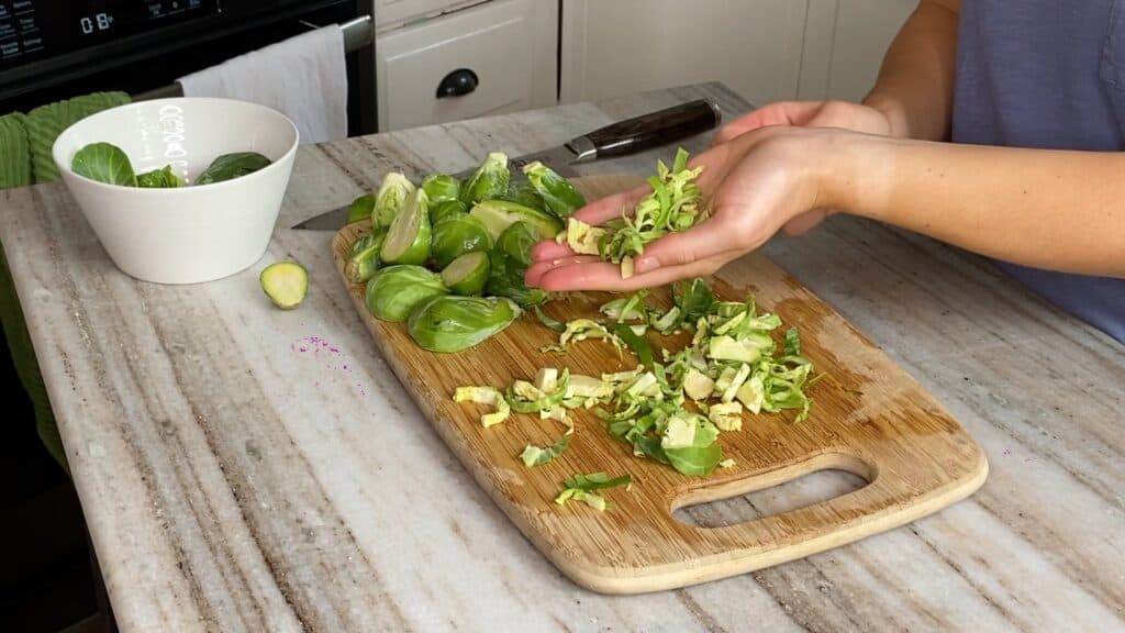 woman holding up shaved brussels sprouts over a bamboo cutting board