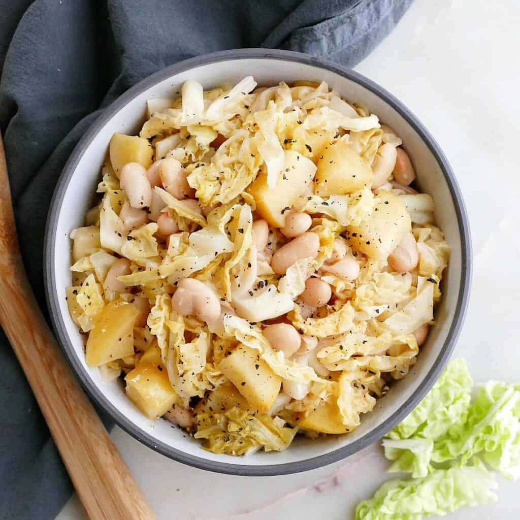 square image of stewed cabbage, apples, and white beans in a serving bowl