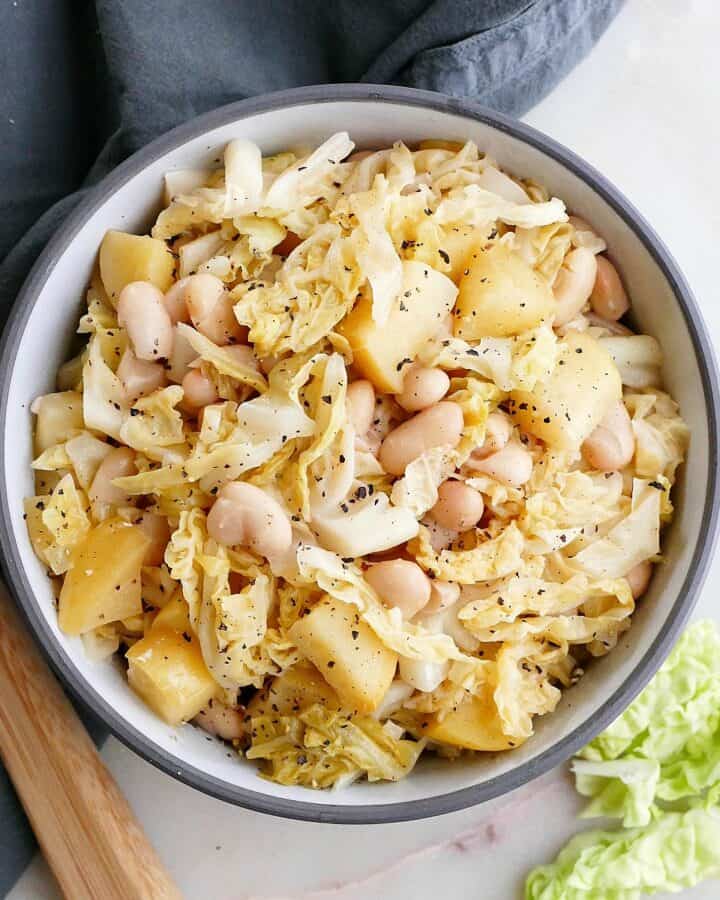 square image of stewed cabbage, apples, and white beans in a serving bowl