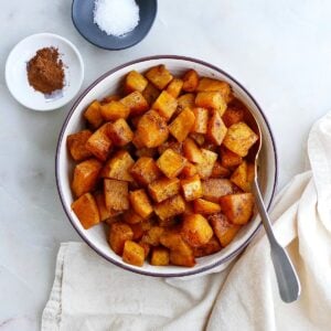 square image of cinnamon roasted butternut squash in a serving bowl on a counter