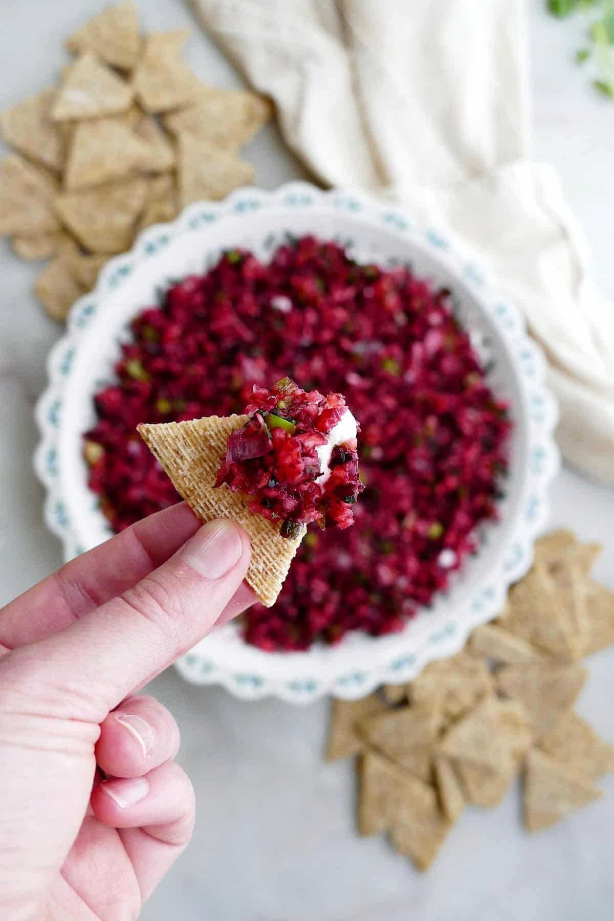 a hand holding a cracker with cranberry jalapeno cream cheese dip over a counter