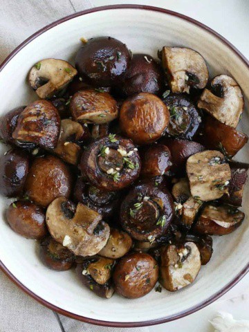 square image of garlic and thyme roasted mushrooms in a serving bowl on a counter