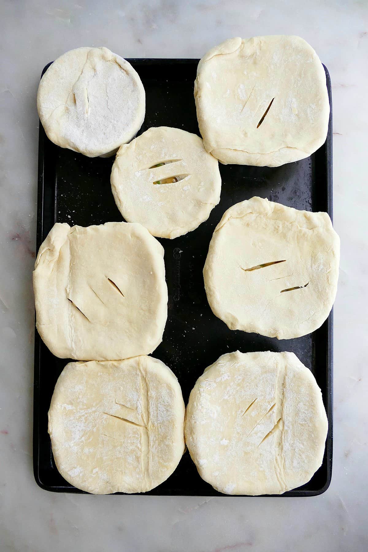 six ramekins filled with pot pie filling and topped with puff pastry on a baking sheet