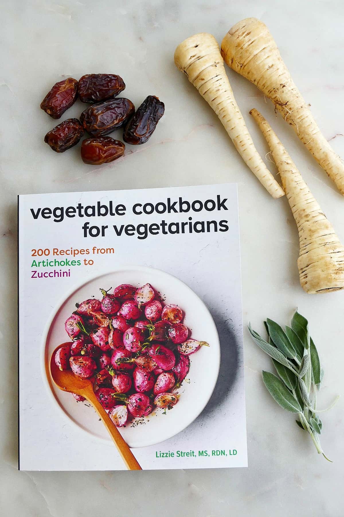 dates, parsnips, and sage leaves on a counter next to a paperback copy of a cookbook