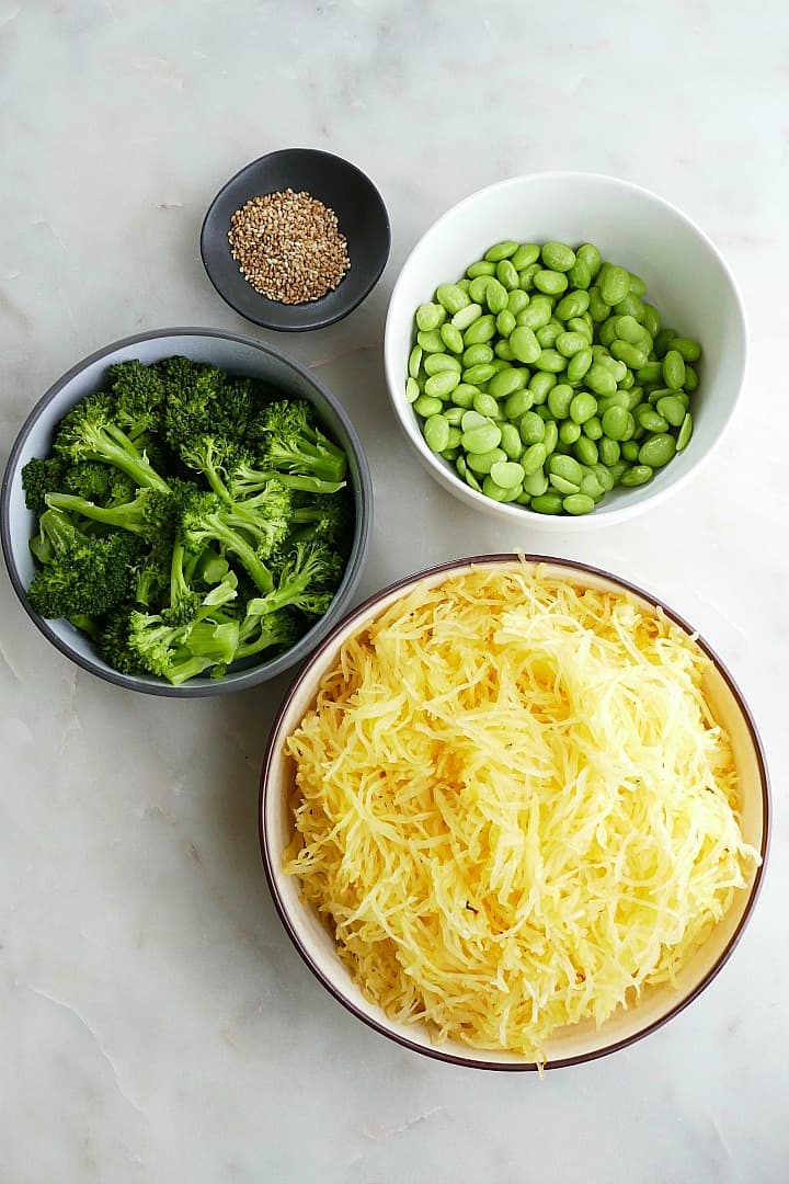 cooked spaghetti squash in a bowl next to broccoli, edamame, and sesame seeds