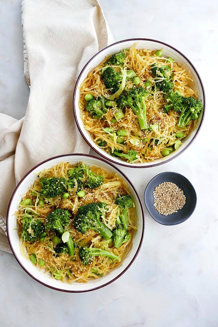 spaghetti squash stir fry in serving bowls on a counter next to sesame seeds