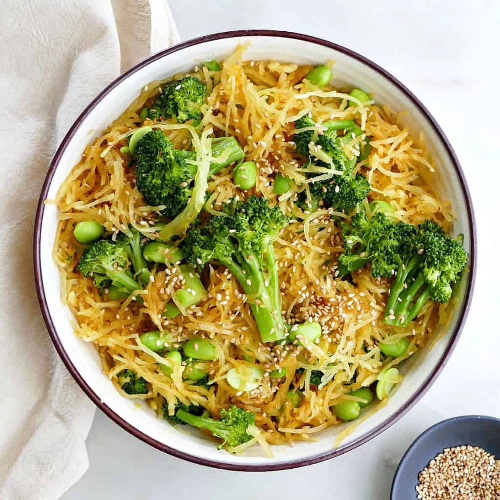 square image of spaghetti squash stir fry with edamame and broccoli in a serving bowl on a counter