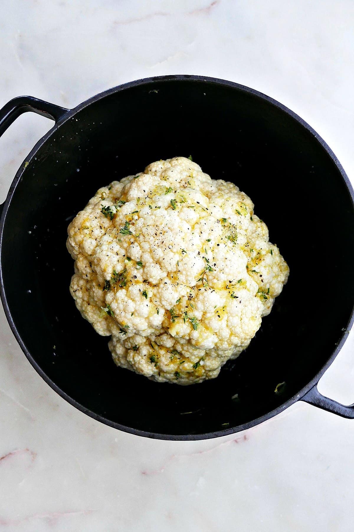 cauliflower head with seasonings in a black Dutch oven on a white counter