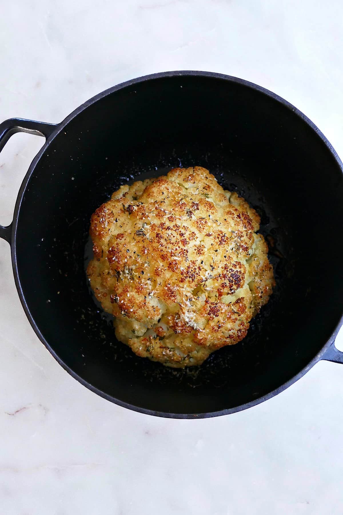 cooked cauliflower head with seasonings in a black Dutch oven on a counter