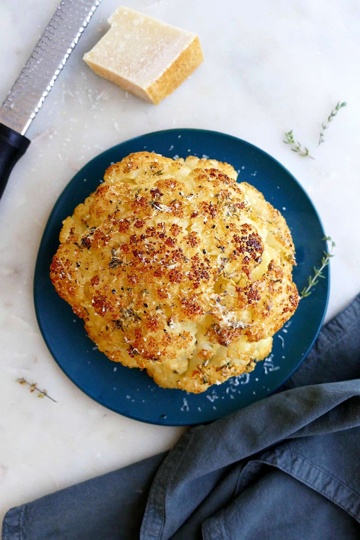 baked whole cauliflower on a serving plate next to parmesan cheese and napkin