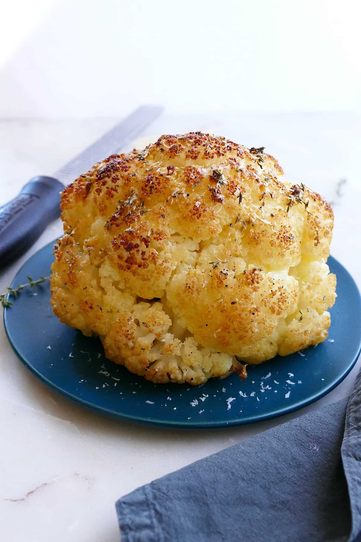 baked whole cauliflower with cheese on a serving plate from the side on a counter