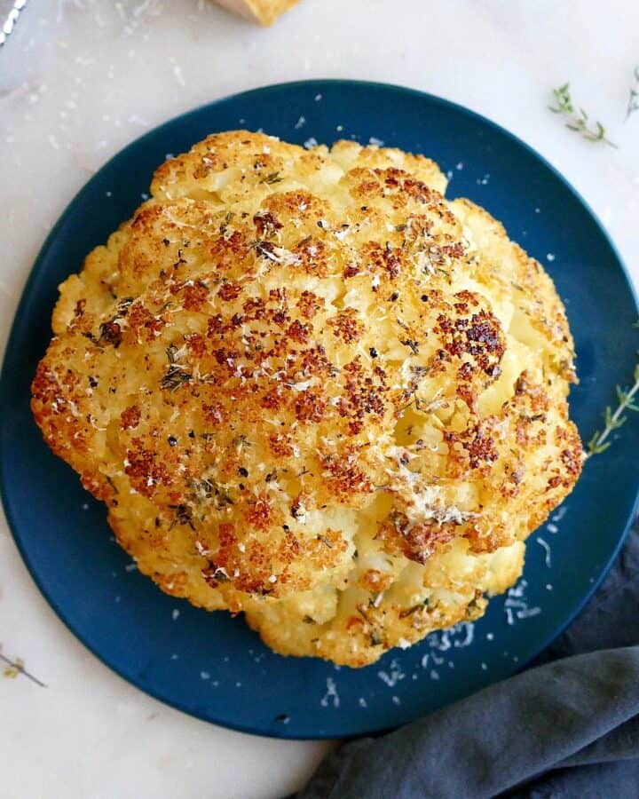 square image of whole roasted cauliflower on a serving plate on a counter